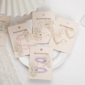 Detailed view of pearl bow and heart hair clips on elegant cream display card