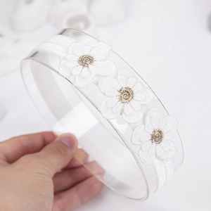 Gros plan sur un bandeau blanc pour bébé avec trois fleurs en dentelle brodée de perles