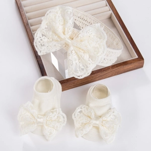 Détail d'un ensemble bandeau et chaussettes en dentelle pour bébé avec nœuds, coloris crème