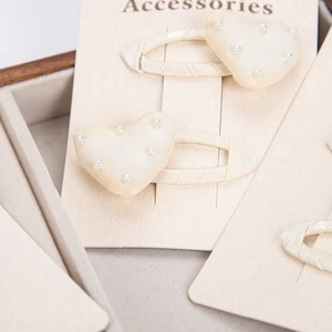 Detail of cream silk heart hair clips with white faux pearls on accessory card