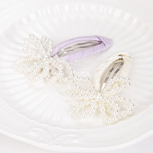Detail of lavender and cream pearl bow hair clips with satin ribbon on a ceramic plate