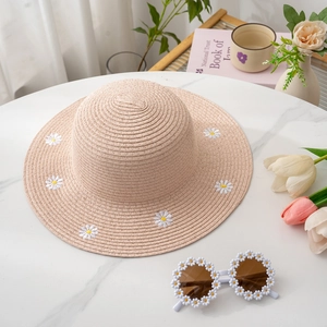 Detailed view of pink straw hat with daisy embroidery and matching floral sunglasses