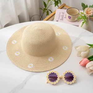Detail of straw hat with daisy embroidery and matching floral sunglasses on a table