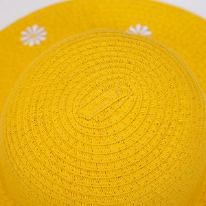 Macro view of yellow woven straw hat featuring detailed white daisy floral appliqués