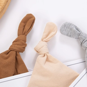 Detail of three knitted baby hats with knot rabbit ears in brown beige and grey tones