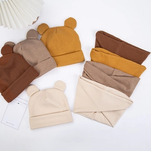 Flat lay of baby bear ear knitted hats and scarves set in warm earth tones on white backdrop