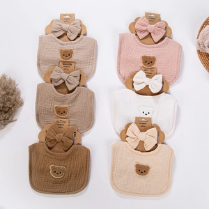 Flat lay of cotton muslin baby bibs and headbands in six soft earthy tones with bear patches