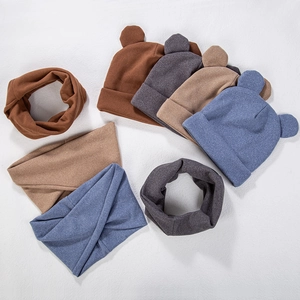 Flat lay of knit bear ear hats and scarves in four colors on a white textured background