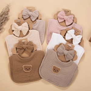 Detail view of cotton muslin baby bib and headband sets in soft earthy colors with bear embroidery