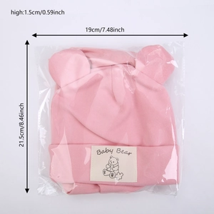 Detailed view of pink baby knit hat with bear ears and dimensions in plastic packaging
