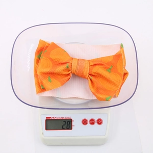 Detail shot of Halloween pumpkin print bow headband weighing 28g on a scale
