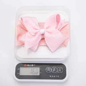 Detail showing pink baby bow headband weighing 16.0g on a scale to show its lightweight feel