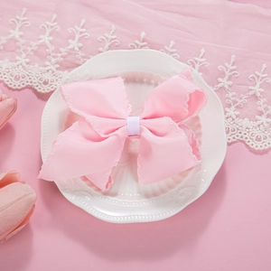 Close-up of pink grosgrain ribbon bow with scalloped edges on a white vintage ceramic plate