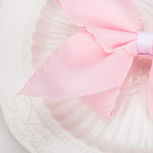 Detail of pink grosgrain bow hair clip with white zigzag stitching on ceramic plate
