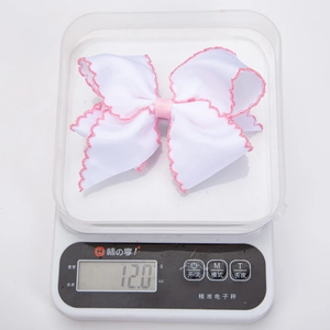 Detail showing the 12.0g weight of the white and pink bow hair clip on a digital scale