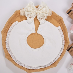 Détail d'un bavoir en dentelle pour bébé et bandeau à nœud sur un plateau décoratif