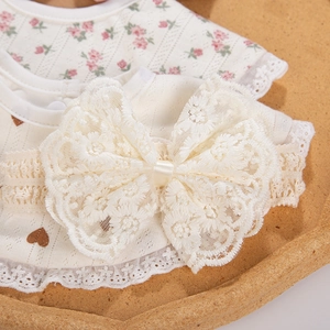 Détail du bavoir en coton pour bébé et bandeau en dentelle avec nœud sur un plateau