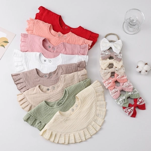 Flat lay of colorful muslin baby bibs with ruffled edges and lace bow headbands