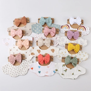 Flat lay of 12 cotton gauze baby bibs and matching bow headbands in soft pastel floral prints