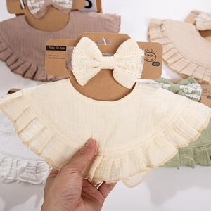 Detail of ruffled cotton baby bib and matching lace bow headband in neutral beige