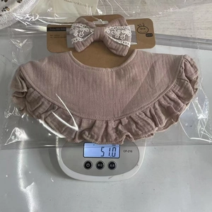 Detail showing baby bib and bow headband set on a scale in clear packaging