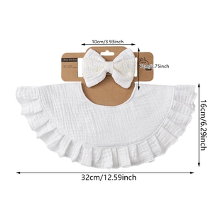 White muslin cotton baby bib and bow headband set with ruffled lace edges on cardboard