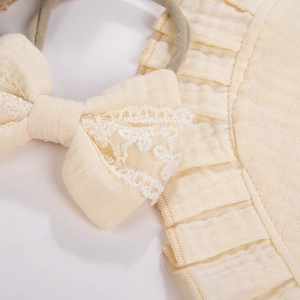 Close-up of cream cotton muslin baby bib with ruffled edges and lace bow headband