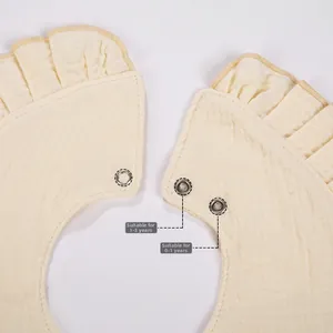 Detail of adjustable metal snaps on ruffled muslin baby bib for ages 0-3 years