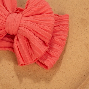 Close-up of coral pink cable-knit baby headband with a large decorative bow