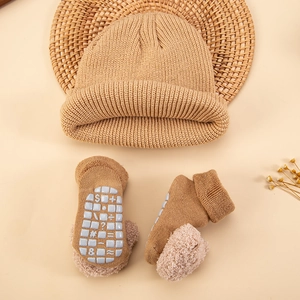 Detail of khaki baby knit socks with non-slip silicone soles and pom-poms on woven mat