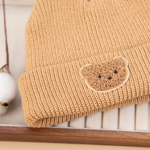 Close-up of caramel knitted baby hat with cute 3D teddy bear patch detail on front