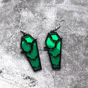 Macro shot of gothic coffin-shaped acrylic earrings with black bat and green translucent base