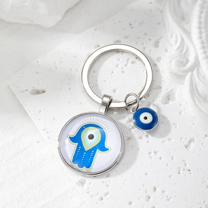 Close-up of Evil Eye Hamsa glass pendant keychain on white textured stone base