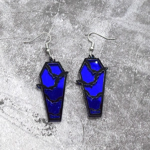 Macro shot of coffin-shaped gothic earrings with blue mirror finish and black bat silhouettes