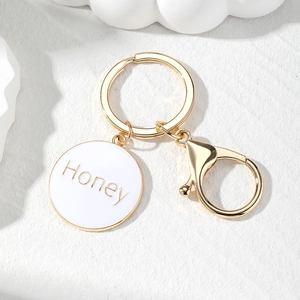 Macro detail of golden Honey letter engraved round charm on a minimalist keyring