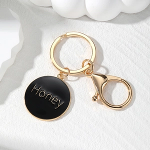 Golden Honey letter heart keychain with black enamel pendant on a white wavy background