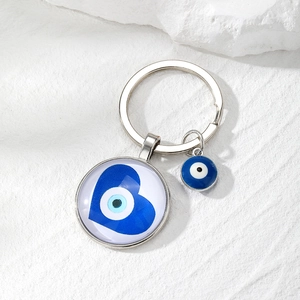 Close-up of heart-shaped evil eye pendant with silver keychain on white stone texture