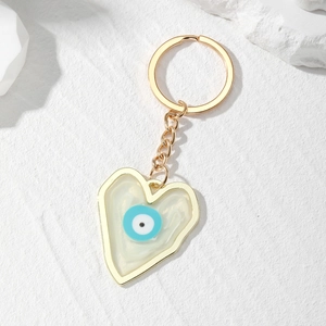 Bohemian gold heart keychain with resin evil eye pendant on a white textured background