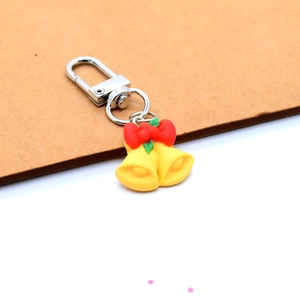 Detailed view of yellow Christmas bell keychain with red bow and green holly leaf charms