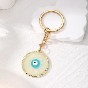Golden Evil Eye keychain with round blue enamel pendant on white marble stone background