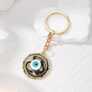 Detailed macro view of the gold-plated evil eye keychain with marble texture background