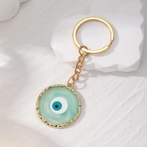 Detailed view of light blue Evil Eye charm keychain with golden alloy wavy frame