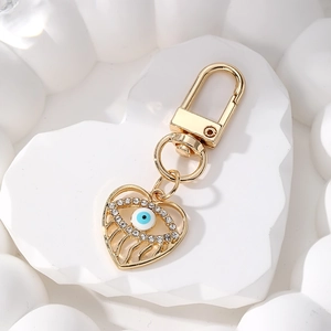 Close-up of golden heart evil eye keychain with sparkling zircons on white heart stone