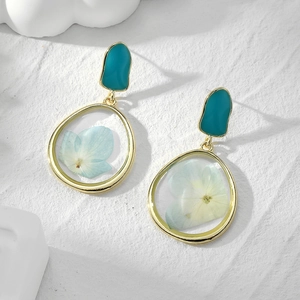 Detailed close-up of gold geometric earrings featuring real blue dried flowers in resin