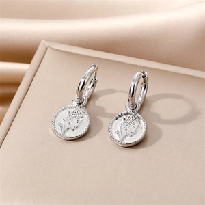 Close-up of silver coin hoop earrings with Queen portrait relief on champagne satin