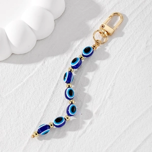 Retro Evil Eye keychain with blue oval beads and gold accents on white texture