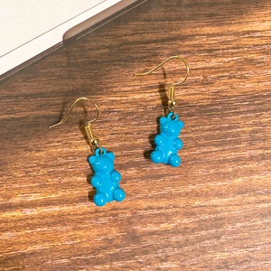 Detailansicht hellblauer Gummibärchen-Ohrhänger mit goldenen Haken auf Holzgrund