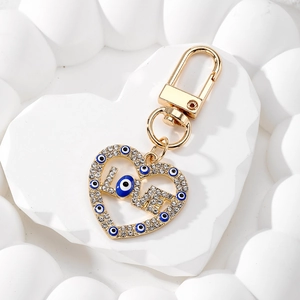 Detail of gold LOVE keychain with rhinestones and evil eye charms on white stone