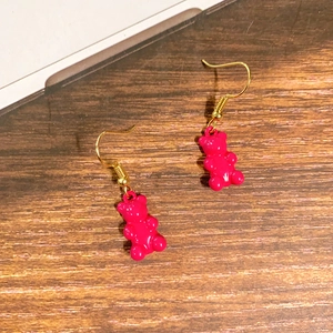 Detailaufnahme der rosaroten Bären-Ohrringe mit goldenen Haken auf Holzhintergrund