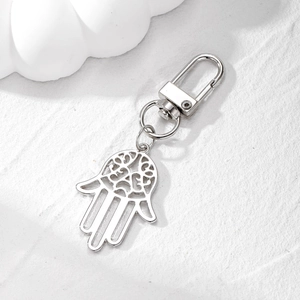 Detailed silver Hamsa hand keychain with intricate hollow carvings on stone texture